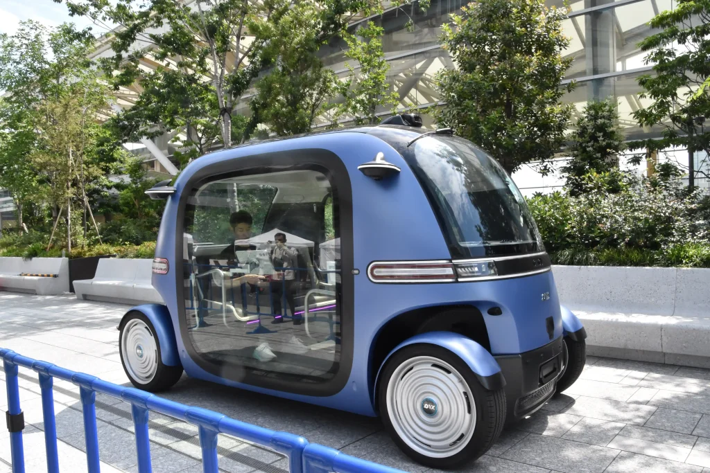 丸みを帯びた青い車の外観。車の窓は大きい。大きい窓から載っている人が見え、コントローラーのようなもので捜査している様子。
